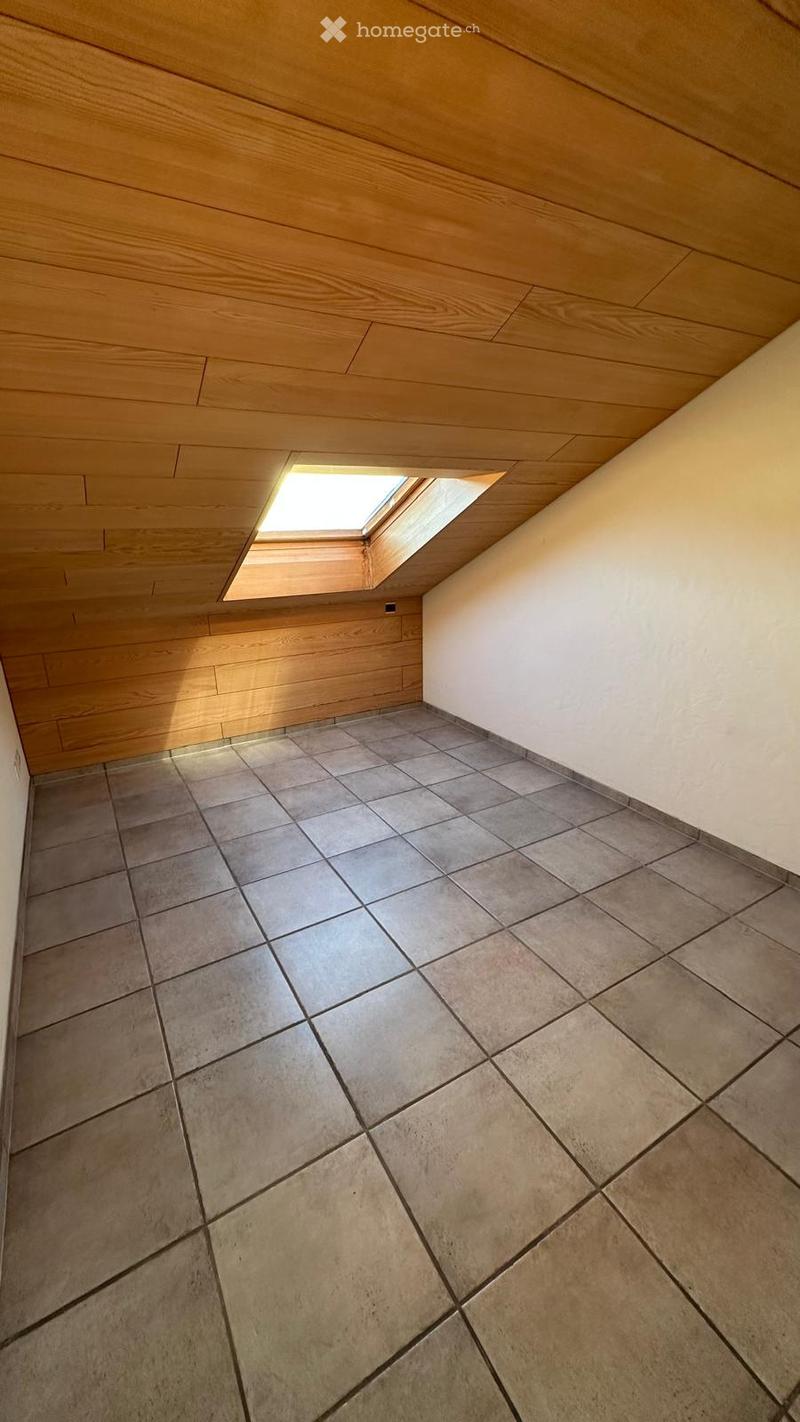 Empty room with tiled floor, wooden ceiling, and a skylight window letting in natural light.