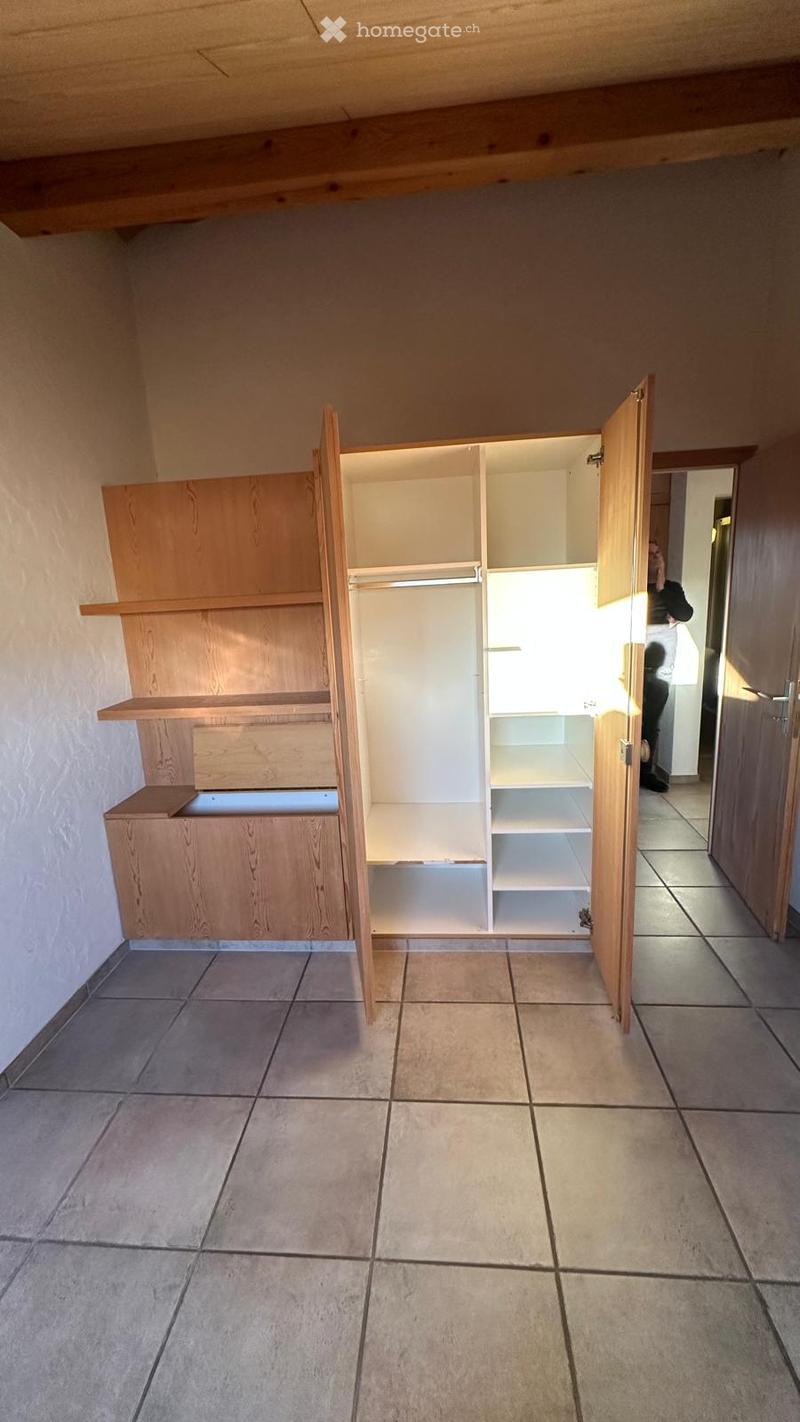 Empty room with tiled floor, wooden built-in closet with open shelves, and a doorway leading to another room.