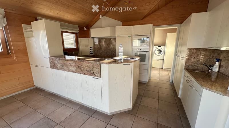 Modern kitchen with white cabinets, granite countertops, and stainless steel appliances including a refrigerator, oven, microwave, dishwasher, and washing machine. The space features a central island with a granite countertop and a window with blinds.