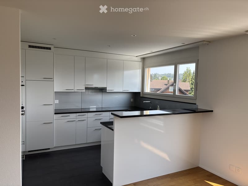 Modern kitchen with white cabinets, black countertops, and a central island. Large windows provide natural light and a view of the surrounding area.