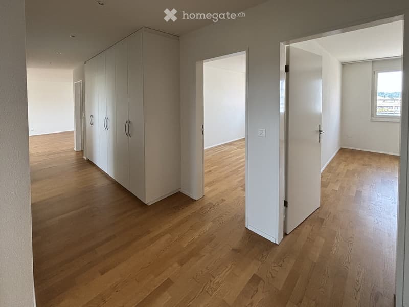 Empty hallway with light wooden flooring, white walls, and built-in white closet units. Open doors lead to adjacent unfurnished rooms.