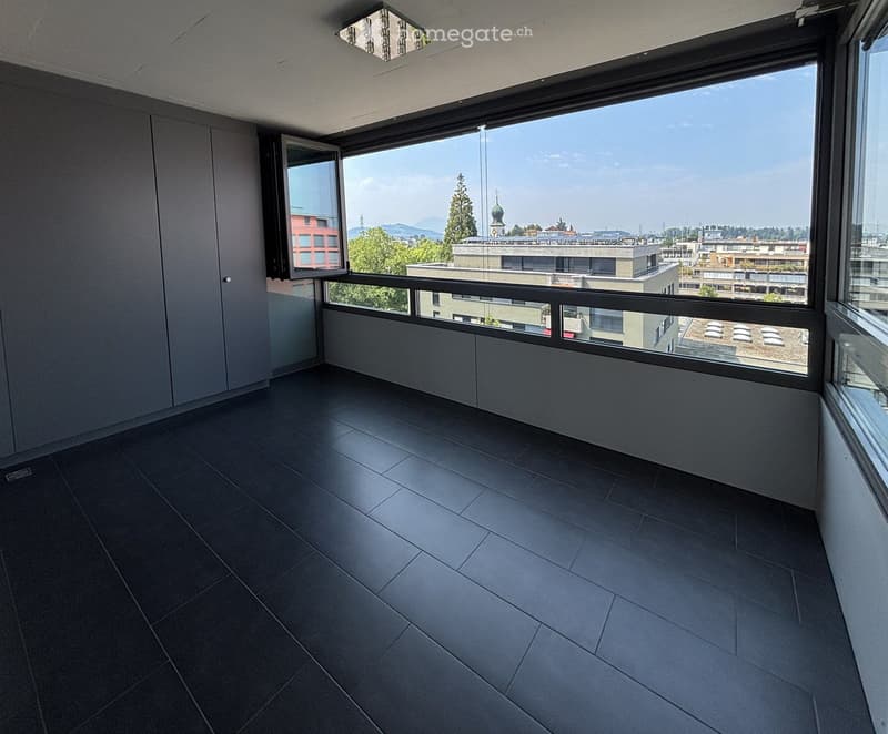 Empty balcony with dark tiled floor, large windows offering a cityscape view, and modern lighting fixtures.