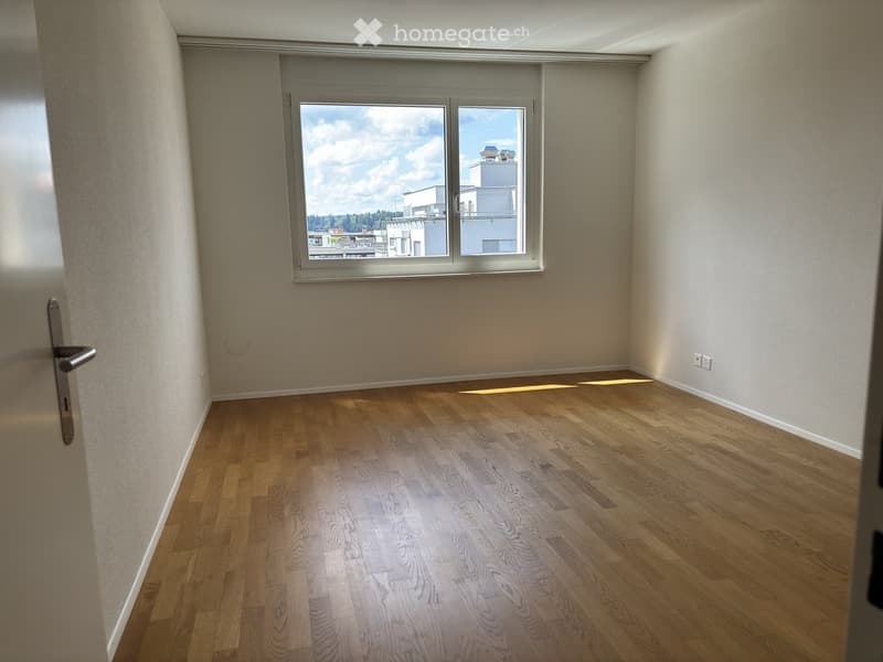 Empty room with wooden flooring, large window, and neutral-colored walls.