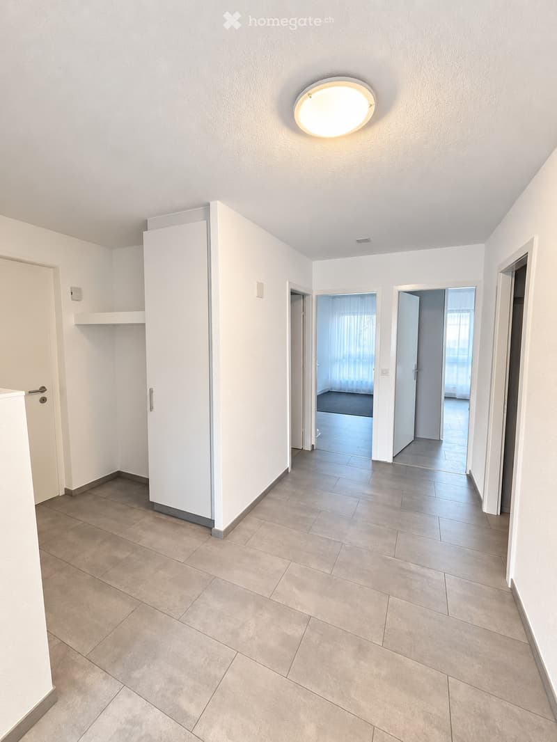 Empty hallway with tiled floor, white walls, and recessed lighting. Doors lead to adjacent rooms.