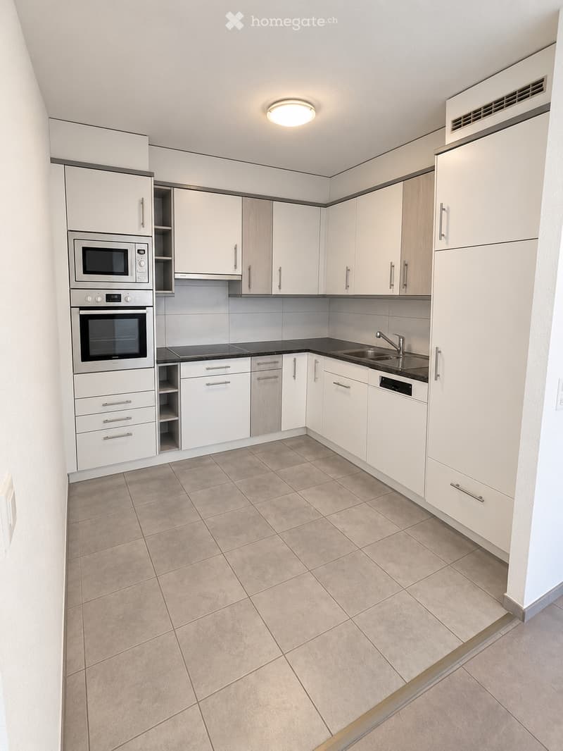 Modern kitchen with white cabinets, stainless steel appliances, and beige tiled flooring.