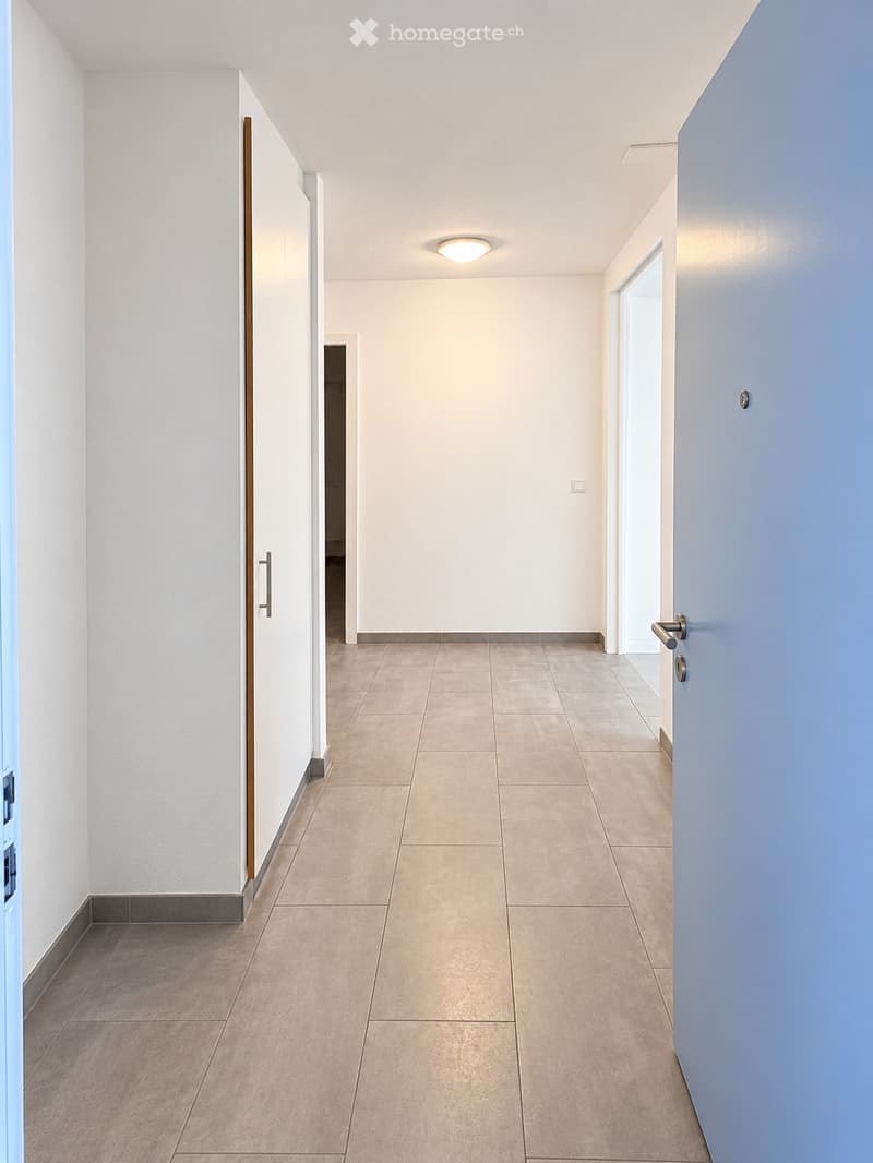 Empty hallway with tiled floor, white walls, and recessed lighting. Doors on both sides lead to other rooms.