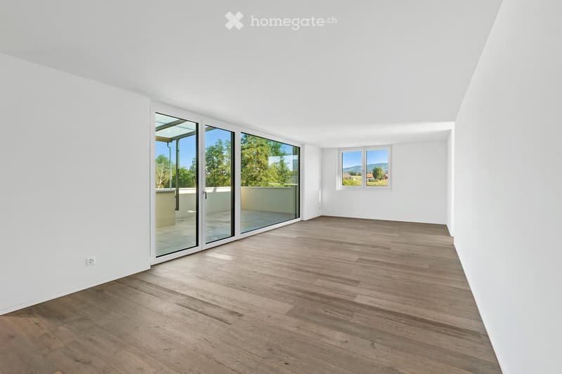 Empty room with white walls, wooden flooring, large sliding glass doors leading to a balcony, and a window with a scenic view.