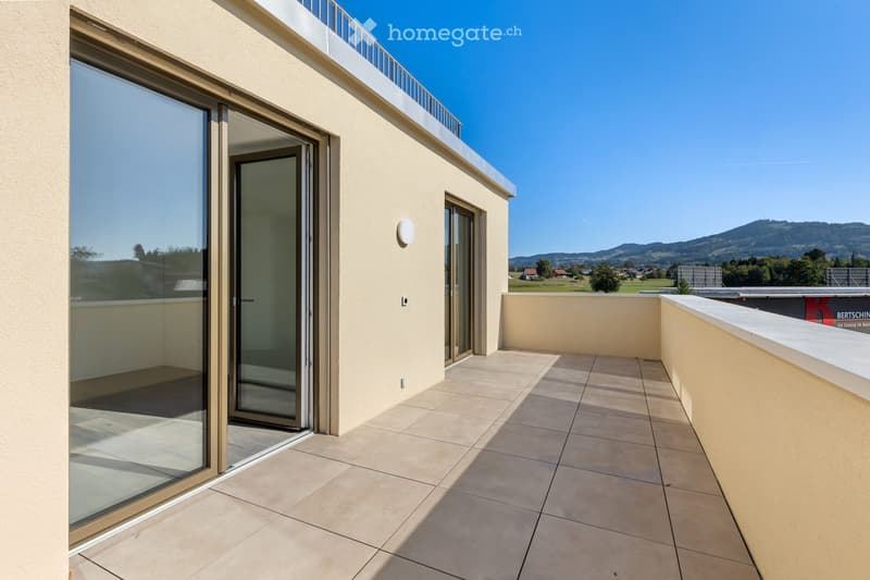 Balcony with tiled floor, glass sliding doors, white wall, and a view of a landscape with mountains and greenery.