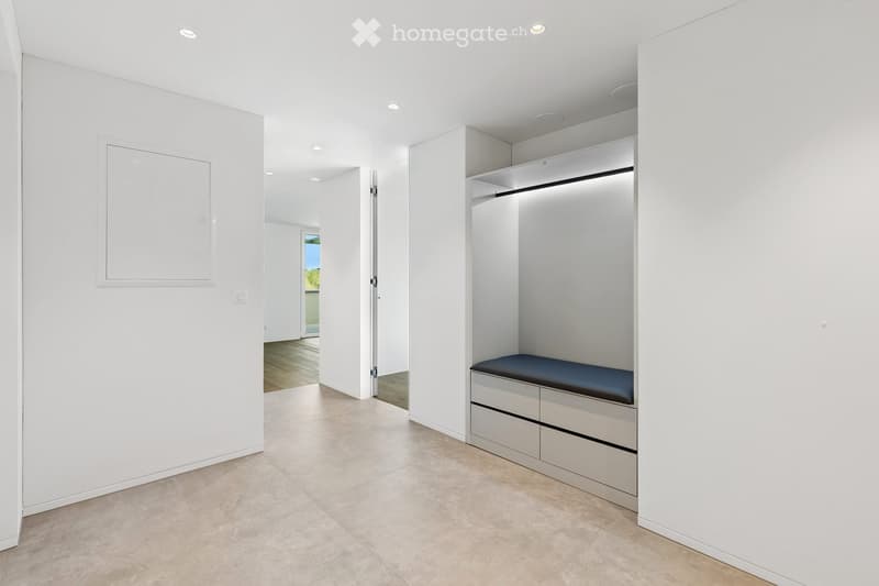 Empty room with white walls, tiled floor, built-in closet with drawers and a bench, and a doorway leading to another space.