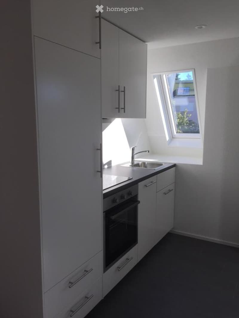 Modern kitchen with white cabinets, a sink, and an oven. The space is bright with natural light coming through a window.
