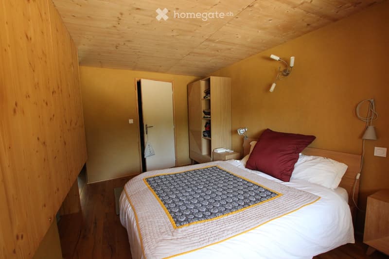 Cozy bedroom with wooden ceiling and warm yellow walls, featuring a neatly made bed with a white quilt and red pillow, a nightstand, and a wooden cabinet.