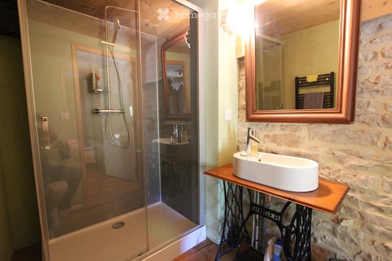 Modern bathroom with a glass-enclosed shower, stone walls, a wooden sink console, and a large mirror.