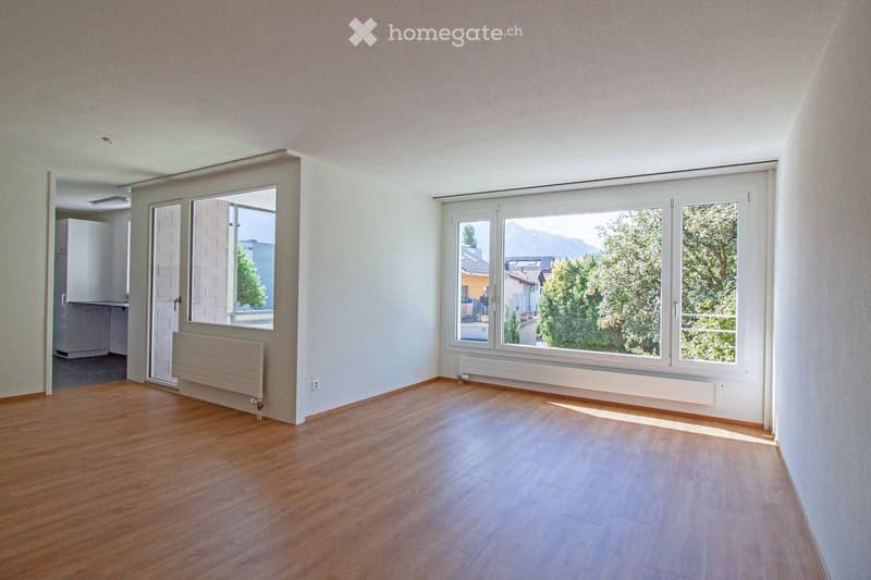 Empty room with wooden flooring, white walls, large windows, and a radiator. No furniture or equipment present.