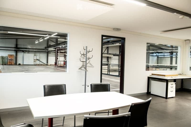 Modern office space with a white table, black chairs, coat rack, and a cabinet with drawers.