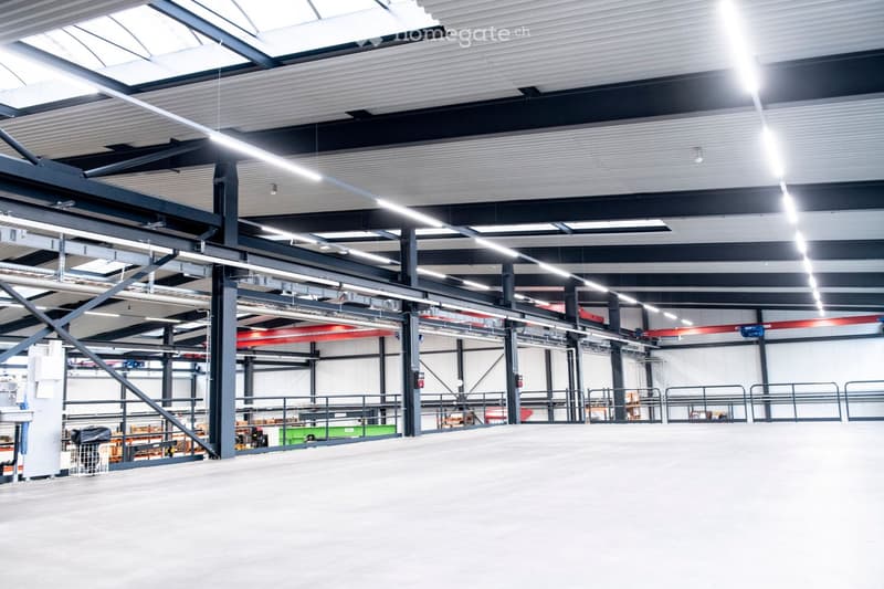 Large industrial-style warehouse with high ceilings, exposed steel beams, and bright lighting. Features include metal railings, storage racks, and a spacious open floor plan.
