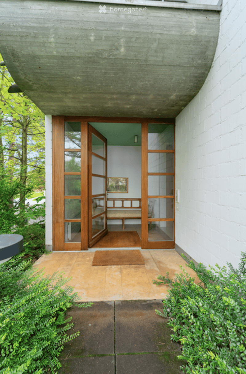 Entrance area with large glass doors leading into a hallway. The hallway features a bench, a framed picture on the wall, and a small rug on the floor.
