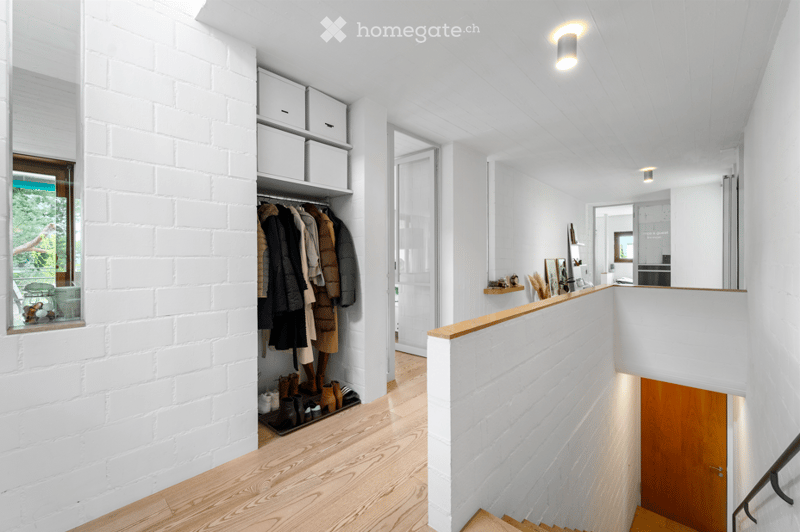 Bright, modern hallway with white brick walls, wooden flooring, built-in storage, coat rack, and a staircase leading upwards.