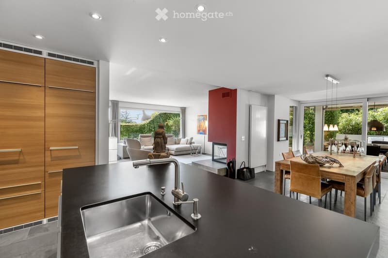 Modern kitchen and living area with a black countertop, stainless steel sink, wooden dining table, and comfortable seating area with a sofa and fireplace.