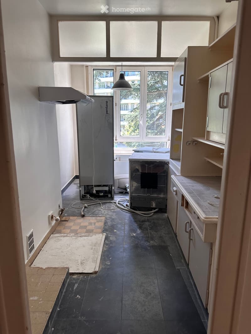 Empty kitchen with white walls, dark tiled floor, and basic cabinetry. No appliances or furniture present.