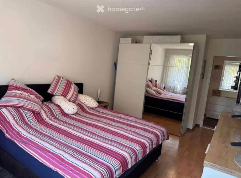 Bedroom with a double bed, colorful striped bedding, pillows, a large mirrored wardrobe, and a nightstand.