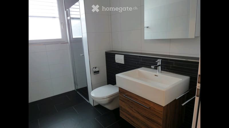 Modern bathroom with white tiles, black accents, a white sink with a chrome faucet, a toilet, and a mirrored cabinet above the sink.