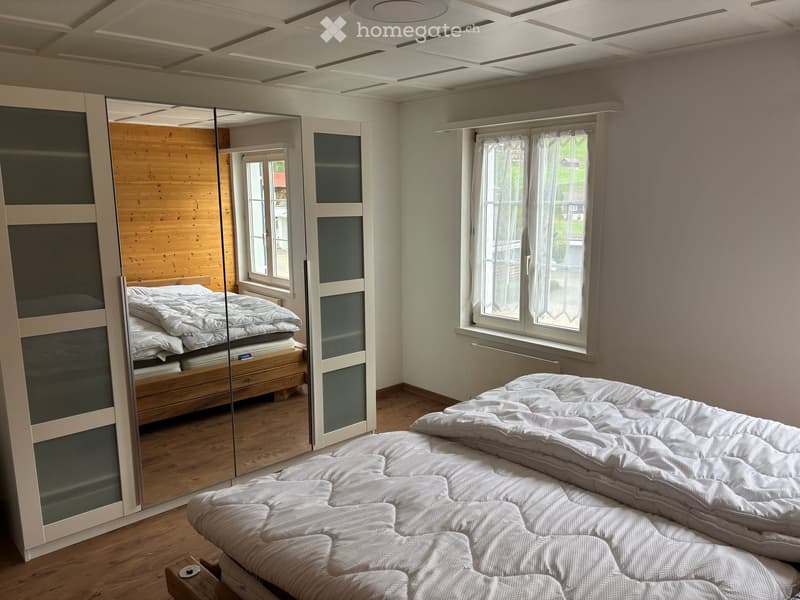 Modern bedroom with a large bed, mirrored wardrobe, and large windows with white curtains.