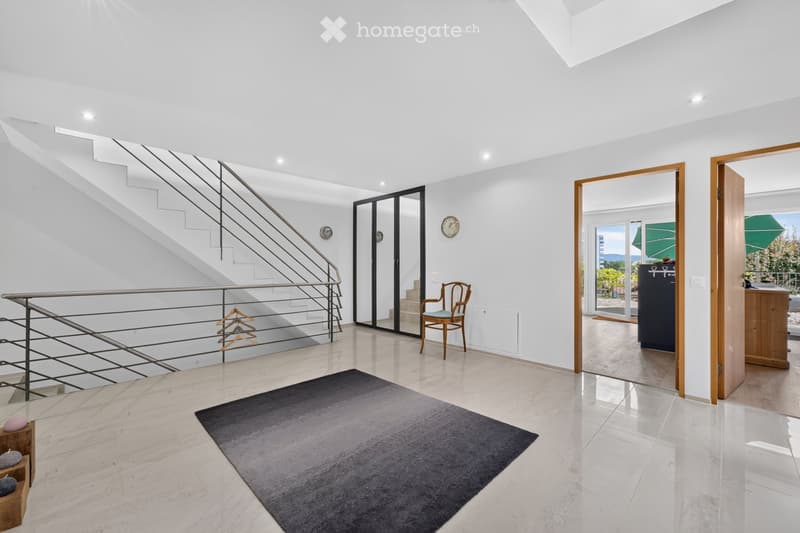 Modern, minimalist hallway with a staircase, a grey rug, a wooden chair, and a coat rack. The space features large windows and a sleek, contemporary design.