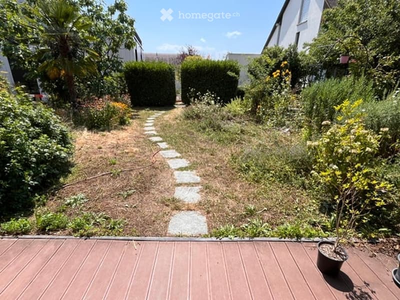 Garden area with a stone pathway, various plants, shrubs, and a wooden deck.