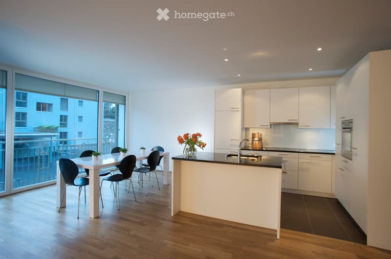 Modern kitchen with white cabinets, black countertops, a central island, a dining area with a table and chairs, and a large window overlooking a balcony.