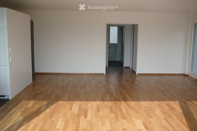 Empty room with light wooden flooring and white walls, featuring a doorway leading to another room.