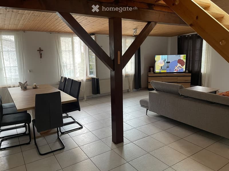 A multi-functional living and dining area with a sofa, dining table, chairs, and a television, featuring wooden beams and large windows.