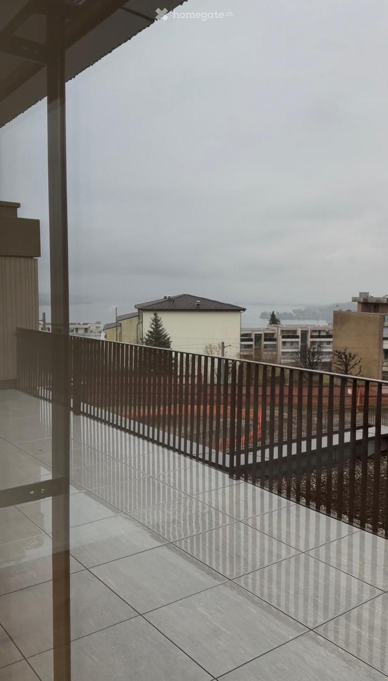 Balcony with tiled floor and metal railing, overlooking a cloudy day with distant buildings and water.