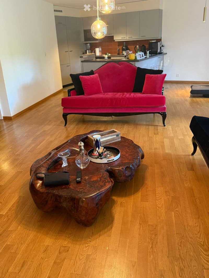 Living room with a red sofa, wooden coffee table, and modern kitchen in the background.