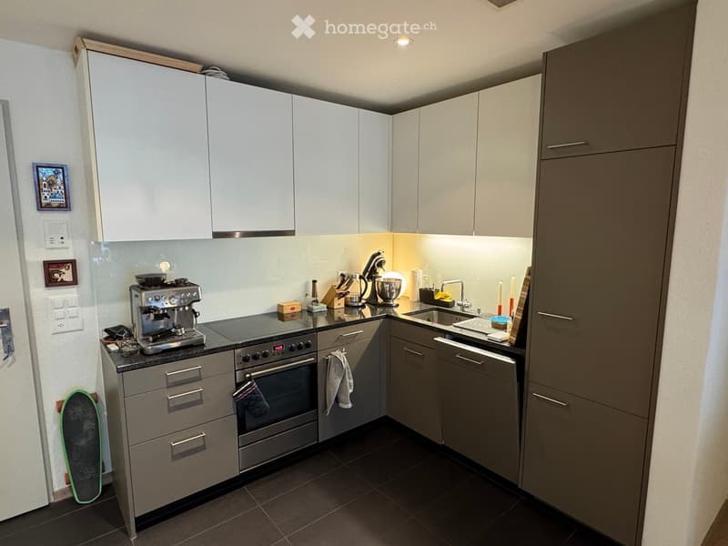 Modern kitchen with white cabinets, stainless steel appliances, and a black countertop. Features include a coffee maker, oven, dishwasher, and sink.