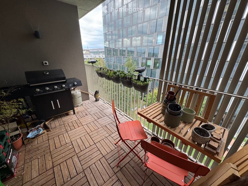 Balcony with wooden decking, barbecue, table with chairs, and potted plants.