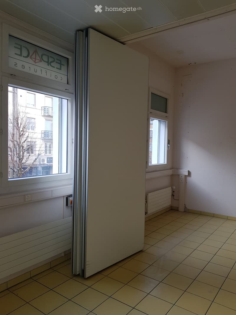 Empty room with sliding door, windows, radiator, tiled floor, and a sign on the wall