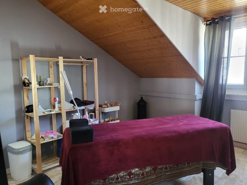 A room with a wooden ceiling, a wooden shelf, a massage table, a trash bin, and a radiator.