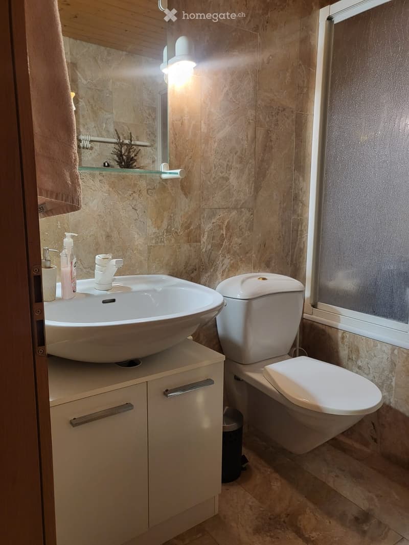 Bathroom with a white sink, white toilet, white cabinet, and a window with a glass door.