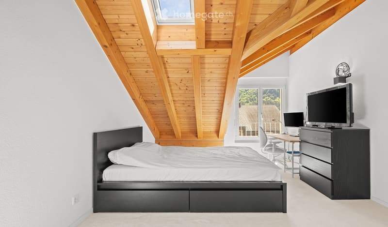 Modern bedroom with a slanted wooden ceiling, large window with a view, bed, desk, chair, laptop, and TV.