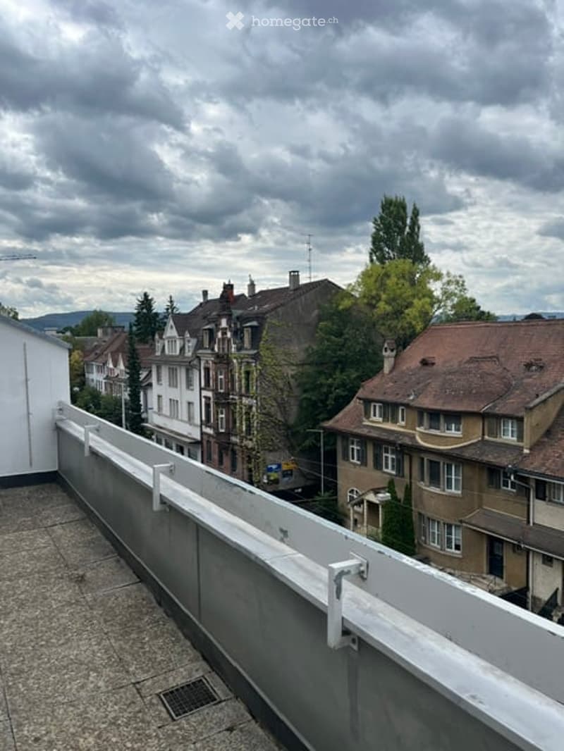 Balcony with white railing overlooking a residential area with multi-story houses and trees.