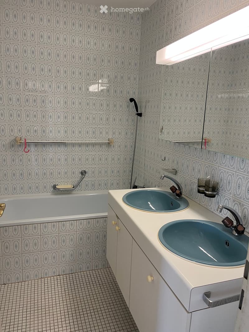 Bathroom with a bathtub, double sink, and decorative patterned tiles on walls and floor.