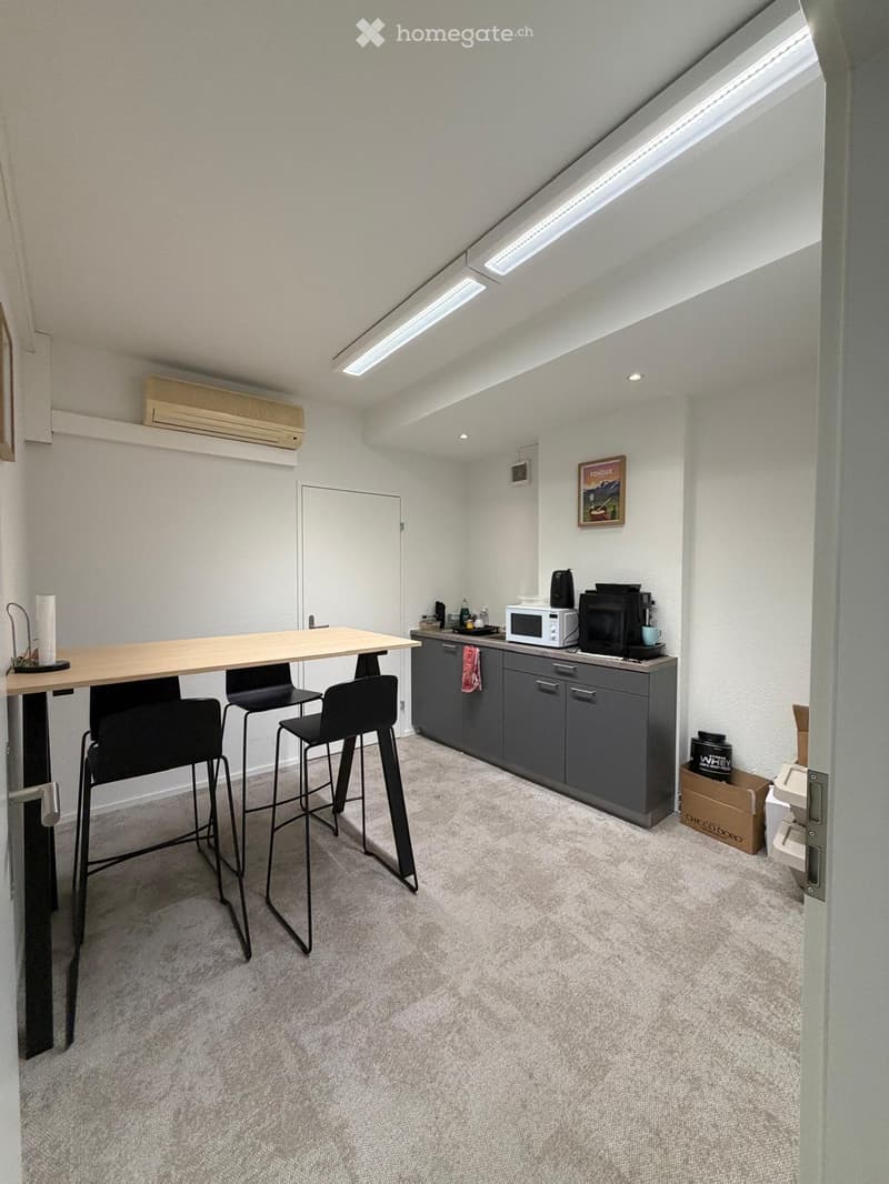 A small, modern kitchen area with a table, chairs, microwave, coffee maker, and cabinets.