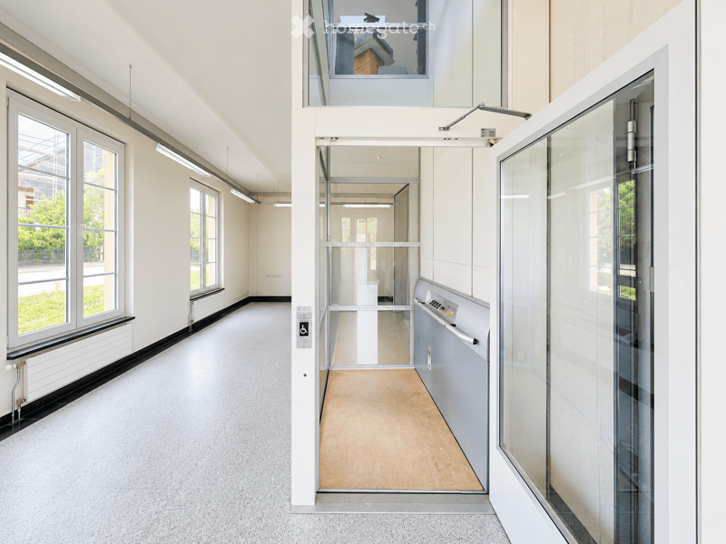 Modern hallway with large windows, glass doors, and a raised platform leading to an upper level.
