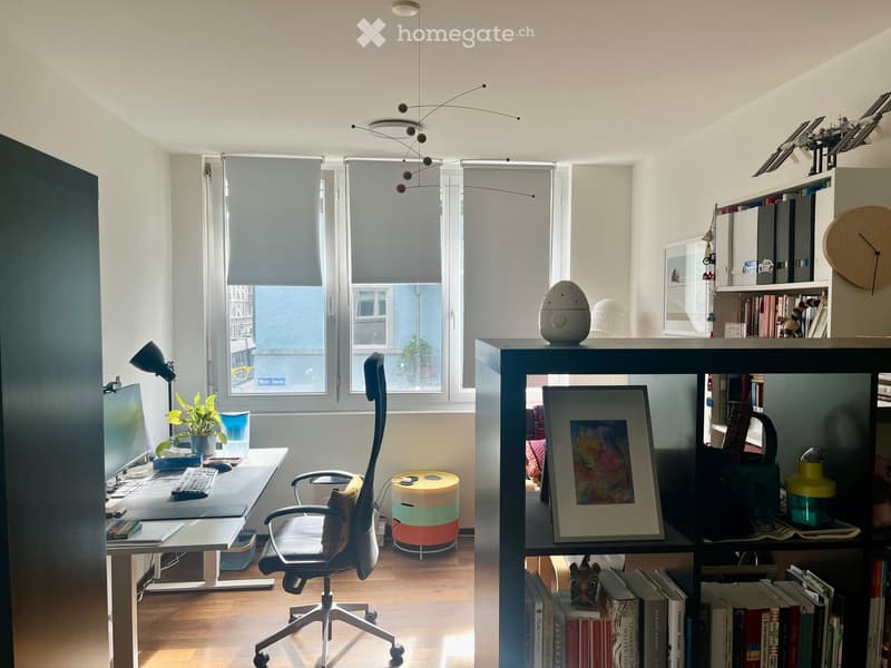 Modern, well-lit office space with a large desk, ergonomic chair, computer setup, bookshelf, and decorative items.