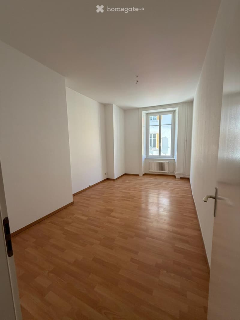 Empty room with wooden flooring, white walls, and a single window with a radiator below it.
