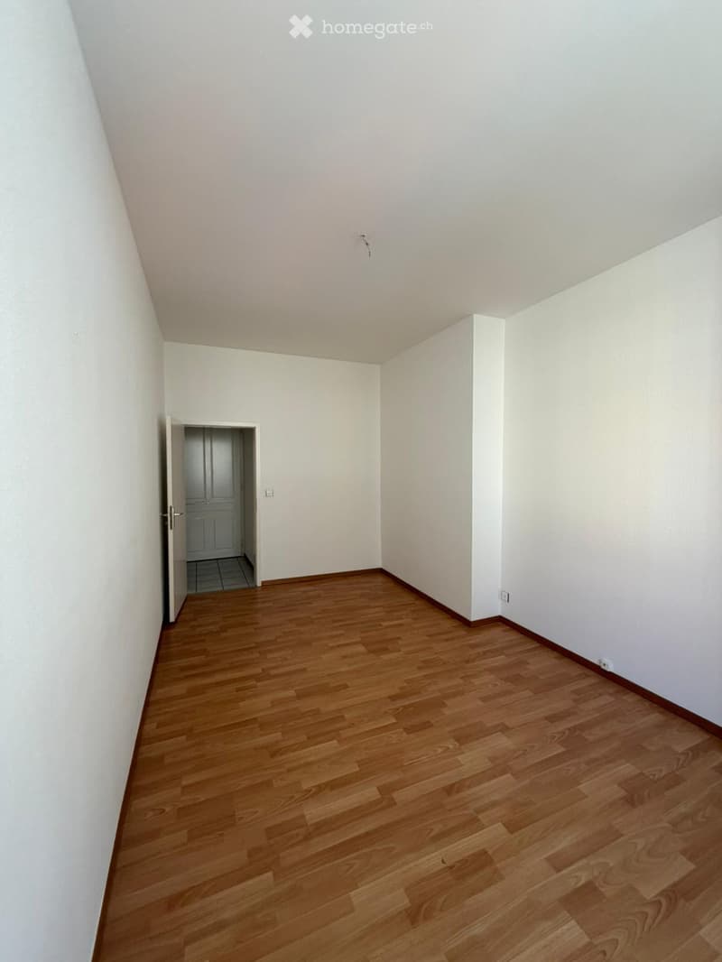 Empty room with wooden flooring and white walls, featuring an open doorway leading to another room.