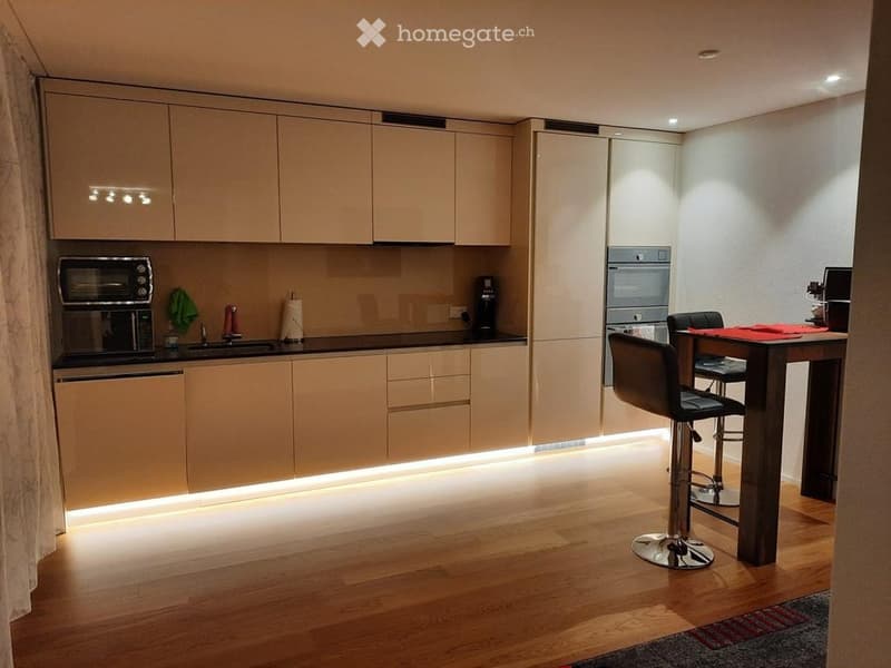 Modern kitchen with light wood cabinets, stainless steel appliances, and a small dining area with a table and stools.