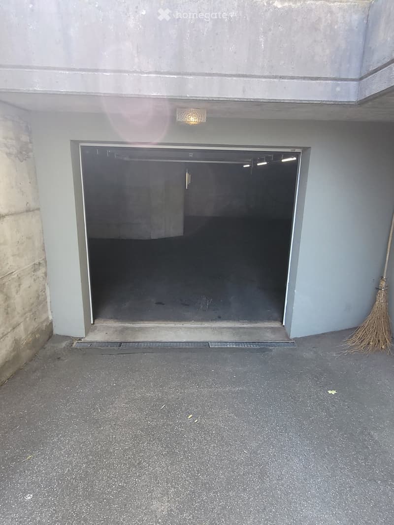 Underground garage entrance with a large, open door and a broom leaning against the wall.