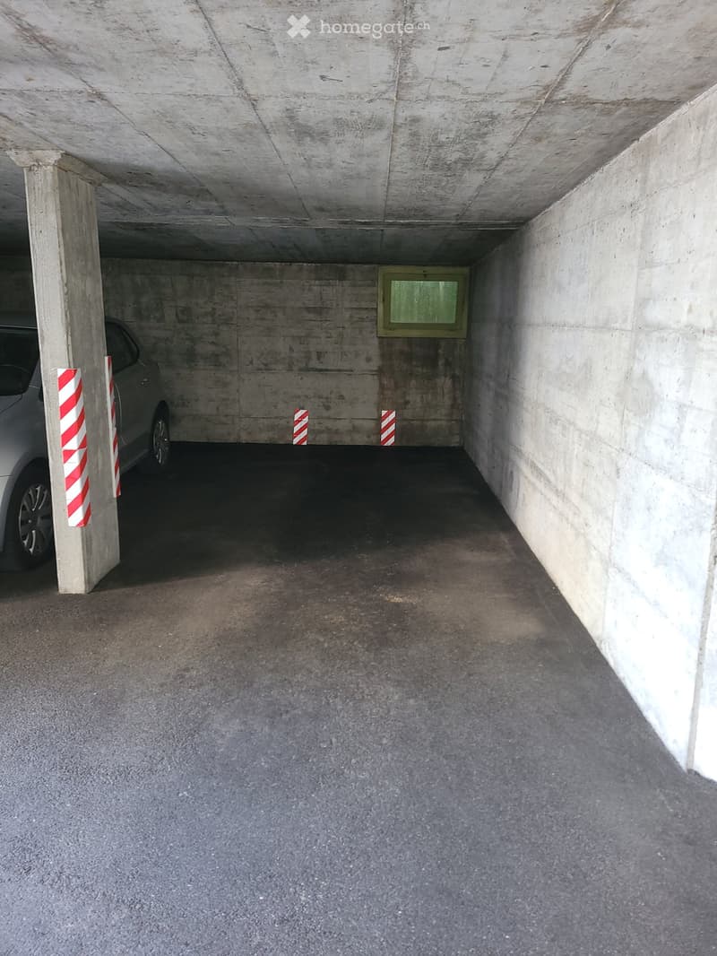 Underground parking space with concrete walls and ceiling, a parked car, and red-and-white striped parking markers.