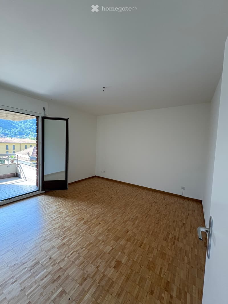 Empty room with wooden flooring, white walls, and a large sliding glass door leading to a balcony.